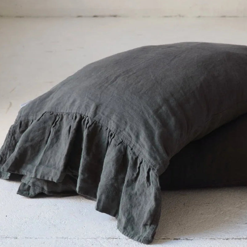 Dark gray ruffled pillow on a light wooden floor.