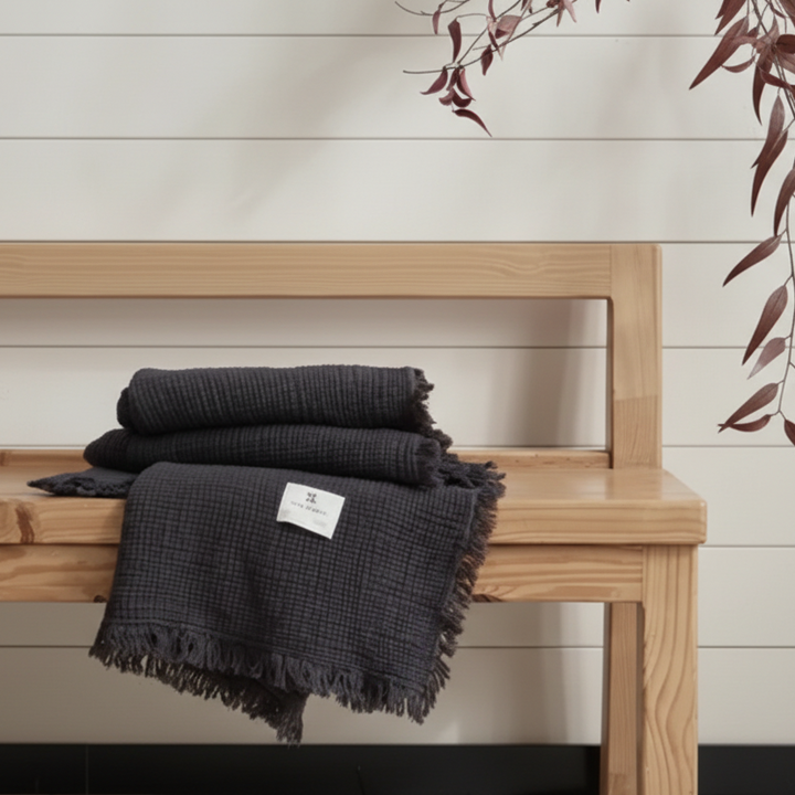 Black textured blanket draped over a wooden bench against a light wood paneled wall.