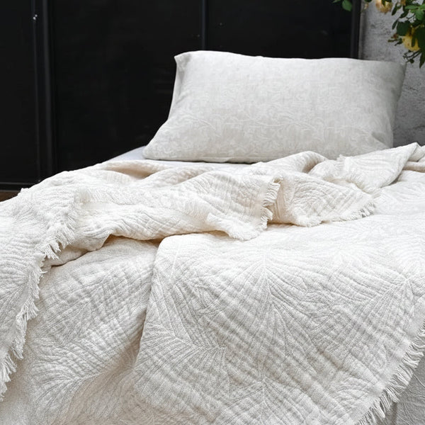 White textured blanket and pillow on a bed with a neutral background