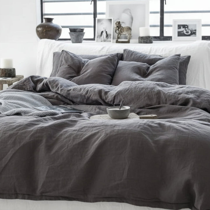 Gray bedding on a bed in a bedroom with a white wall and window.