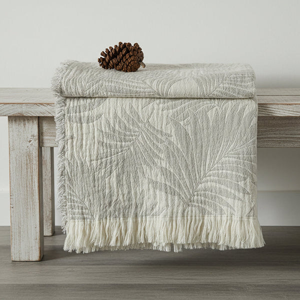 Textured white blanket with leaf pattern draped over a wooden surface.