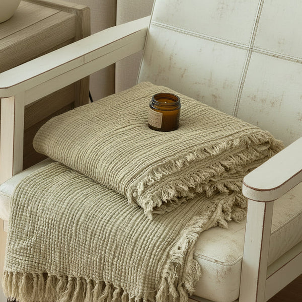 Beige blanket draped over a brown leather chair with a wooden side table and decorative item in the background.