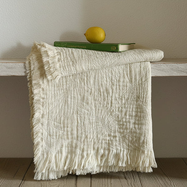 Textured white blanket draped over a wooden surface with a lemon and book on top.