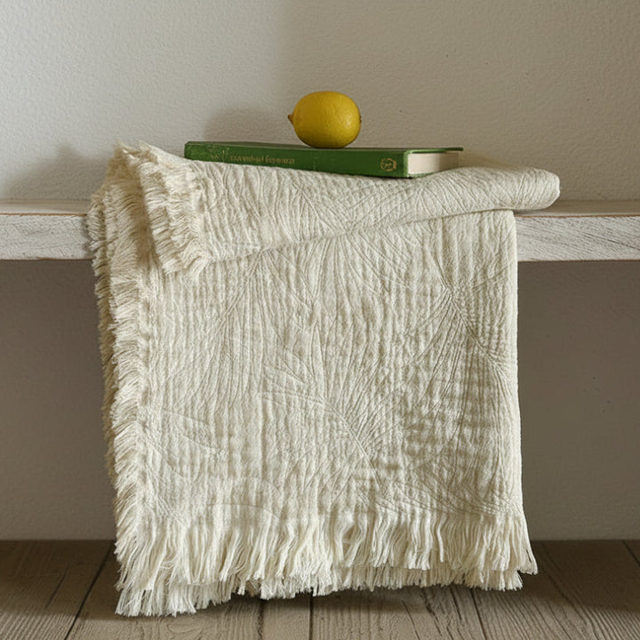 Textured white blanket draped over a wooden surface with a lemon and book on top.