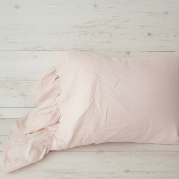 Pink textured comforter on a bed with a woven basket at the foot of the bed.