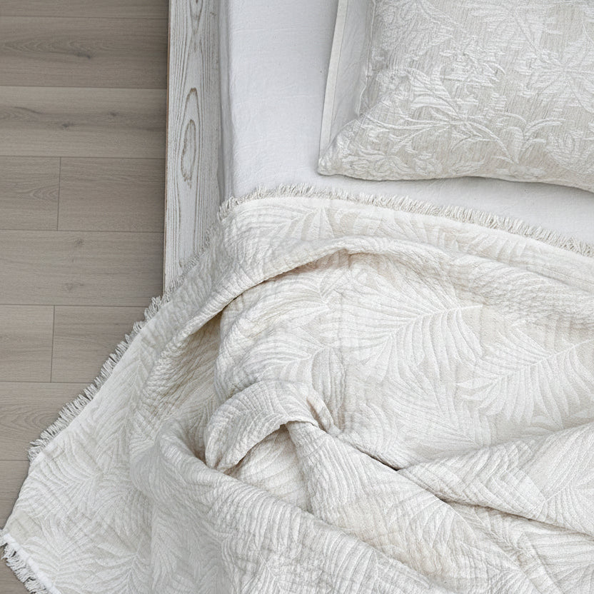 Close-up of textured white bedding on a bed with a concrete floor background